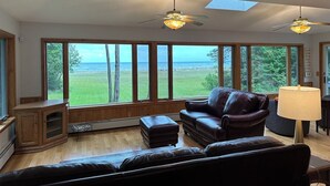 A spacious living room with a large window offering a view of the ocean, a ceiling fan, and a leather sofa.