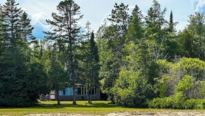 A cabin surrounded by dense forest, with a clear sky above.