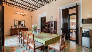 A dining area with a green tablecloth, wooden chairs, a chandelier, and a ceiling with exposed beams. - Espectacular casona con alberca y jardines (Mérida)