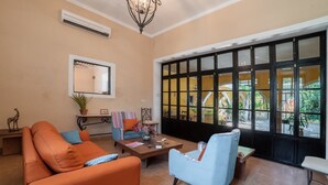 A living room with a sofa, armchair, coffee table, and a large window with a view of the outside. - Espectacular casona con alberca y jardines (Mérida)
