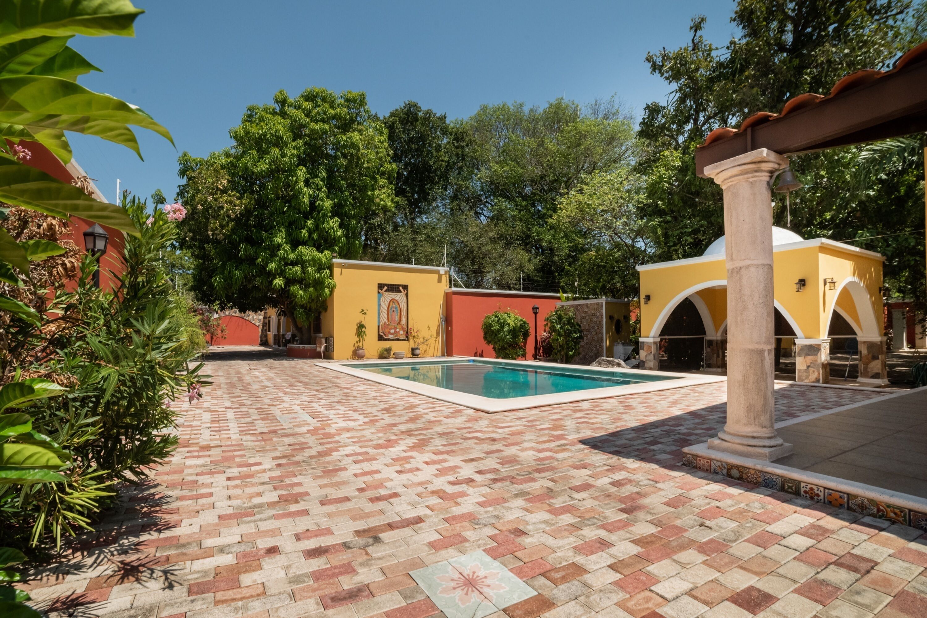 A courtyard with a swimming pool, tiled flooring, and a yellow building with arches.
