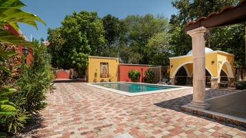 A courtyard with a swimming pool, tiled flooring, and a yellow building with arches.