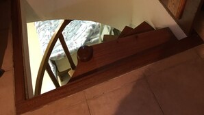 Un escalier en bois, agrémenté d’un panneau de verre, mène à une pièce dont le lit est recouvert d’une couvre-lit à motifs floraux.