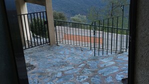 Un balcon dallé de pierres, avec une balustrade en métal, offrant une vue sur un paysage montagneux.