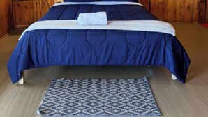 Une chambre avec un mur lambrissé en bois, un lit avec une literie bleue, un tapis à motifs, une lampe suspendue verte et une lampe sur pied.