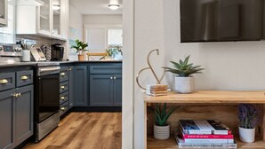 Una cocina moderna con armarios gris oscuro, horno empotrado y encimera de madera. Se observa una estantería con libros y una planta en maceta.