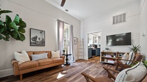 Una sala de estar con un sofá marrón, piso de madera, un televisor y una cocina al fondo.