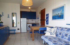A compact living space with a kitchenette, dining area, and a sofa with patterned upholstery. - Holiday apartment directly on the beach (Porto Santa Margherita)