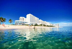 A beachfront hotel with multiple high-rise buildings, clear blue water, and a sandy beach.
