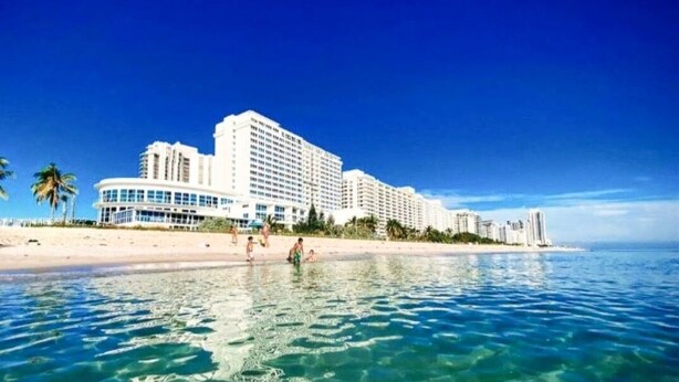 A beachfront hotel with multiple high-rise buildings, clear blue water, and a sandy beach. - Castle 1118 Studio BayView Pool, Direct Beach Access, Tennis, Gym, Free Parking (Miami Beach)