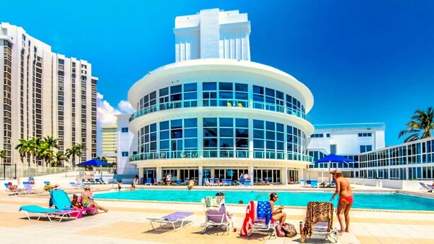 A hotel with a pool area, multiple lounge chairs, and a large building with a curved facade. - Castle 1120 Cozy Studio with Intercoastal View, Free Parking, Tennis, Pool, Gym, Beach Access (Miami Beach)