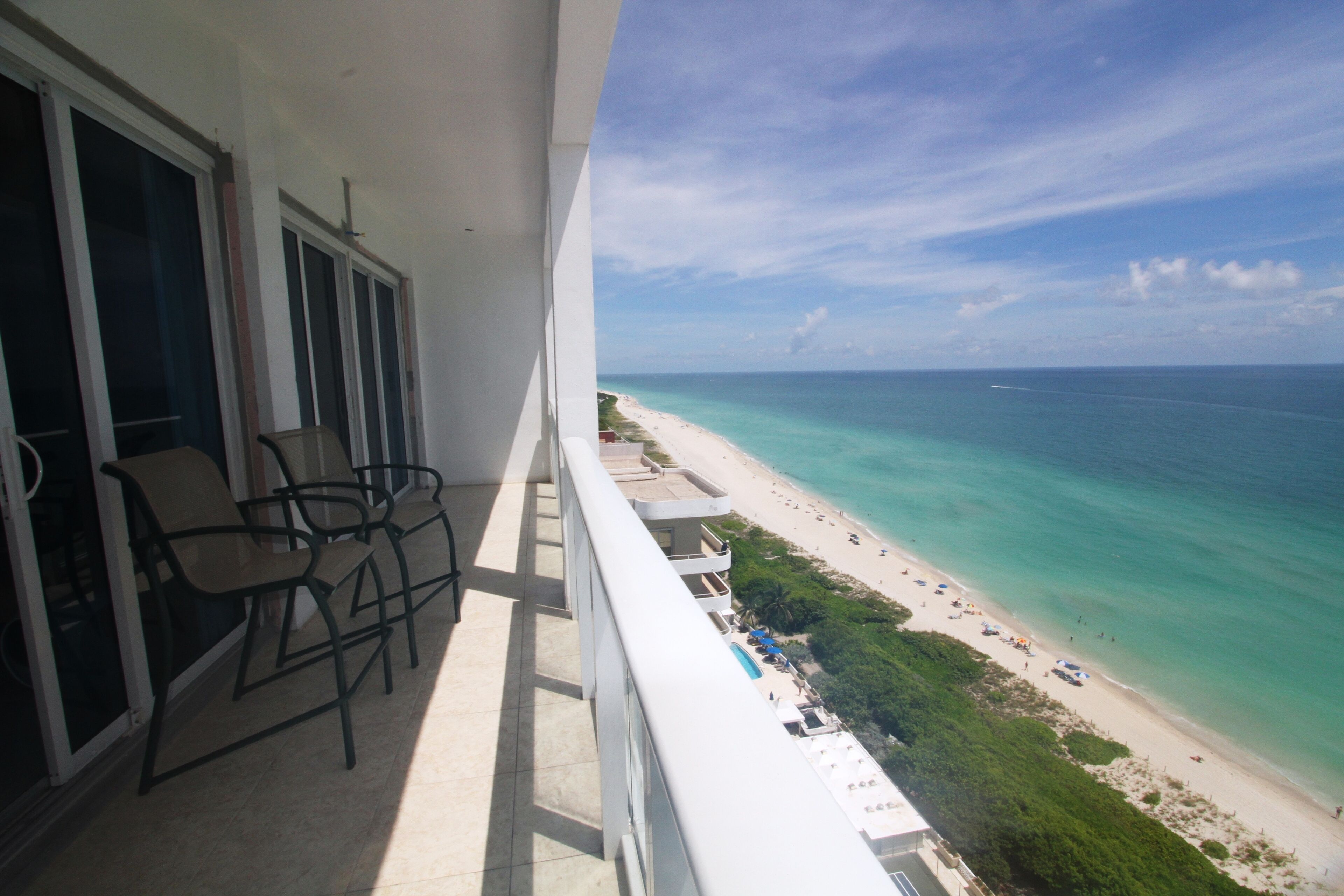 A balcony with chairs overlooking a beach and ocean.