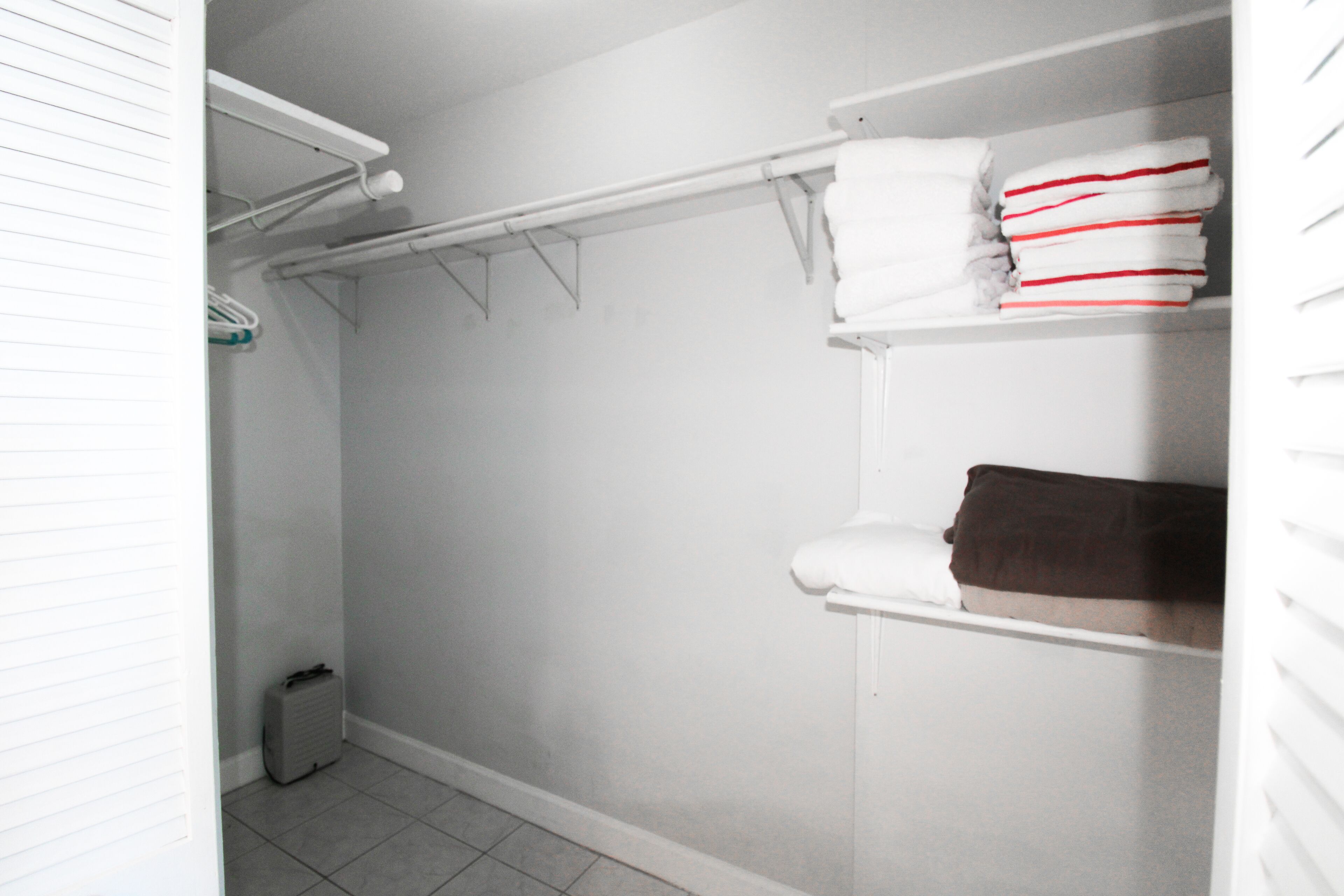 Ein Badezimmer mit weiß gefliestem Boden, einer weißen Toilette, einem weißen Waschbecken und einem weißen Handtuchhalter mit Handtüchern.