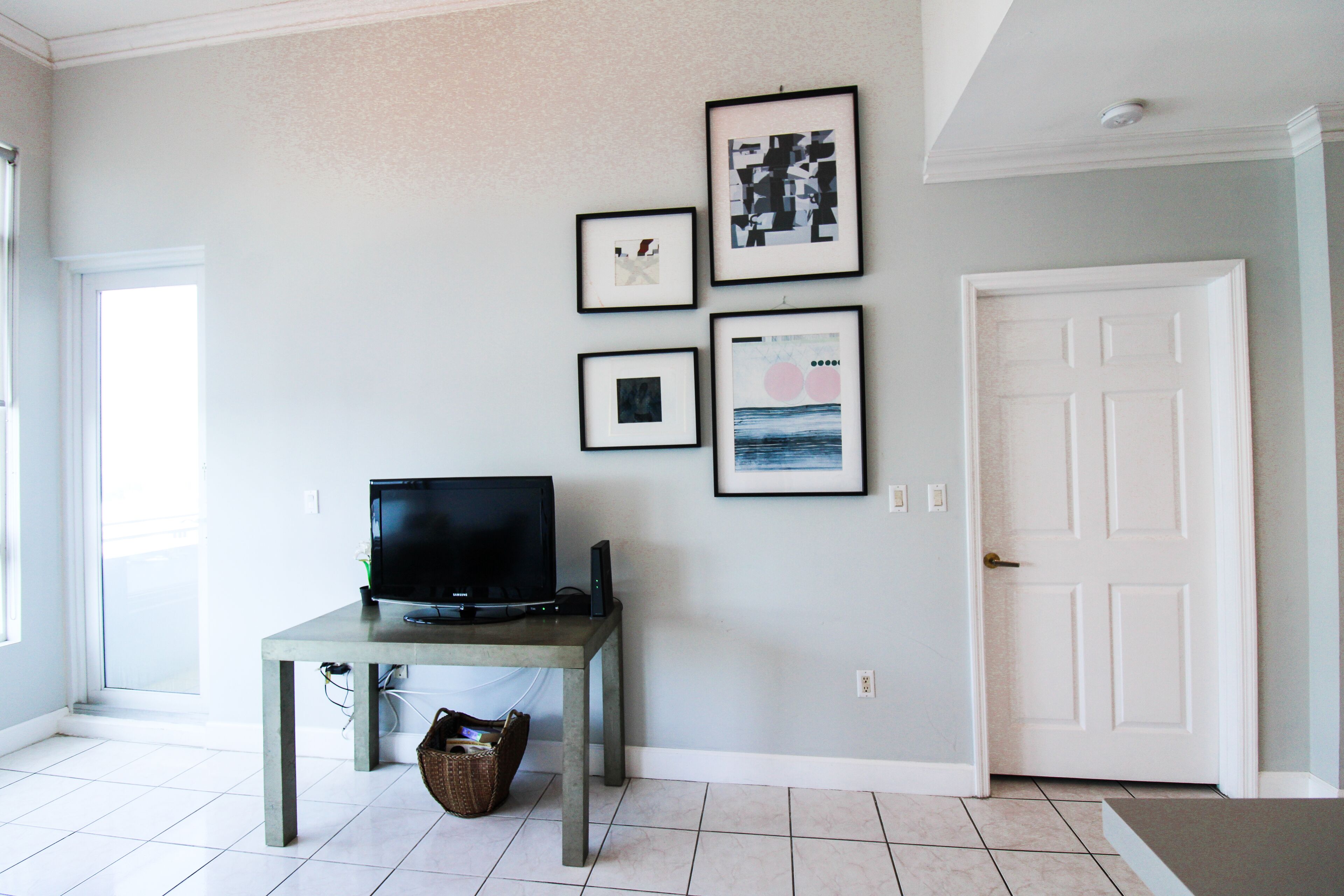 A room with a television on a table, a door, and framed pictures on the wall.