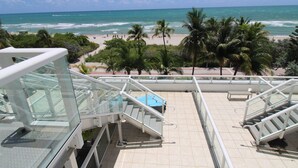 A view from a balcony overlooking a beach with palm trees, a staircase, and a pool.