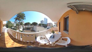 Una vista panorámica de un balcón con una mesa y sillas blancas, una planta pequeña en maceta y vistas de la ciudad.