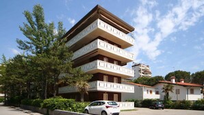 Un edificio de varios pisos con balcones, rodeado de árboles y coches estacionados.