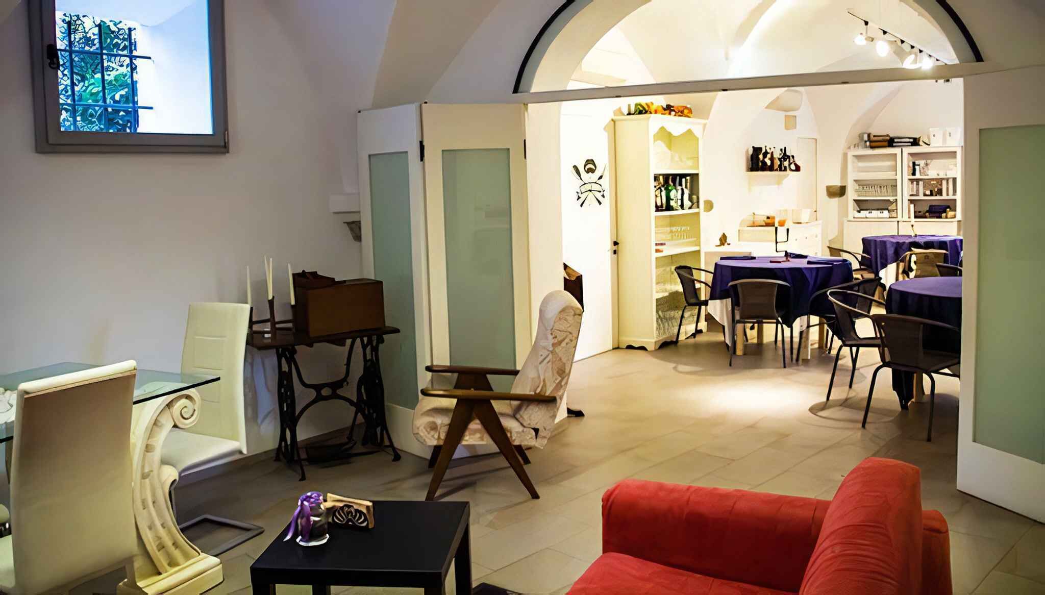 Un salon avec un canapé rouge, une table en verre et un fauteuil blanc. On y trouve également un coin repas avec une table et des chaises, ainsi qu’une cuisine équipée d’étagères et d’un réfrigérateur.