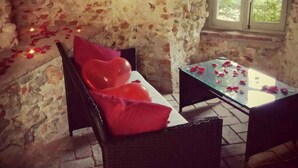 Ein Zimmer mit Steinwänden, einer Bank, einem Tisch mit Rosenblüten und einem Fenster.