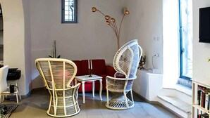 Ein Wohnzimmer mit einem roten Sofa, zwei Korbstühlen, einem kleinen Tisch und einem Bücherregal.