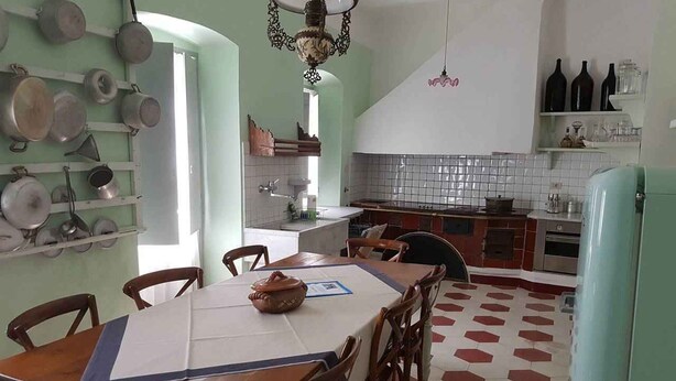 Cuina amb taula de menjador, cadires i diferents olles i paelles penjades a la paret.