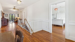 A spacious room with hardwood flooring, a white railing, a staircase, and a bed with a white headboard.