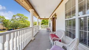 A covered porch with white wicker furniture and a white railing.