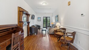 A spacious living room with hardwood flooring, a wooden desk, a sofa, and two armchairs.