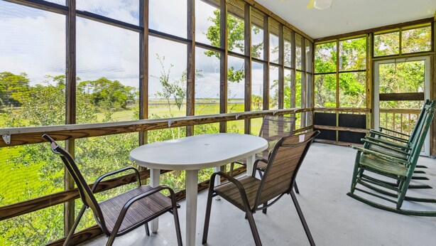 A covered patio with a table and chairs, large windows, and a ceiling fan.
