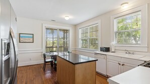 A kitchen with wooden flooring, white cabinetry, a central island, and a dining area with chairs.
