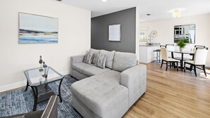 A modern living room with a grey sofa, a glass coffee table, and a painting on the wall.