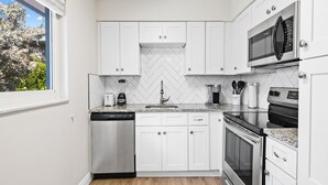 A modern kitchen with white cabinets, a dishwasher, a coffee maker, and a microwave.