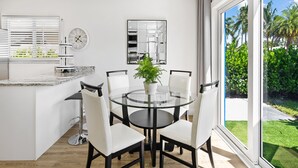 Una cocina moderna con una mesa redonda de vidrio, sillas blancas, un reloj y un ventanal que ofrece vistas a la vegetación.