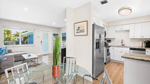 Una cocina moderna con armarios blancos, electrodomésticos de acero inoxidable y una mesa de comedor de vidrio.
