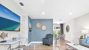 Una sala moderna con un televisor de pantalla plana grande, un comedor con mesa de vidrio y una zona de estar acogedora con sofá y sillones.