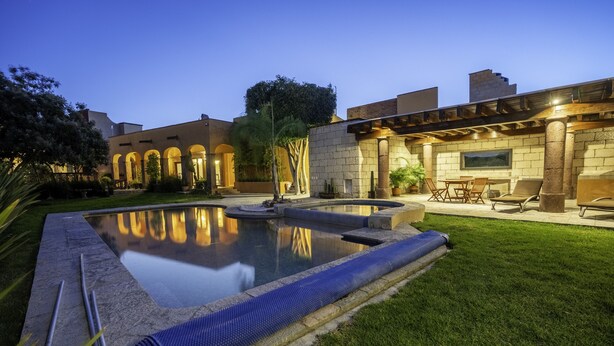 A well-maintained outdoor pool area with a stone deck, a hot tub, and a patio with chairs and a table. - Angelic Centro 2BR with Pool (San Miguel de Allende)