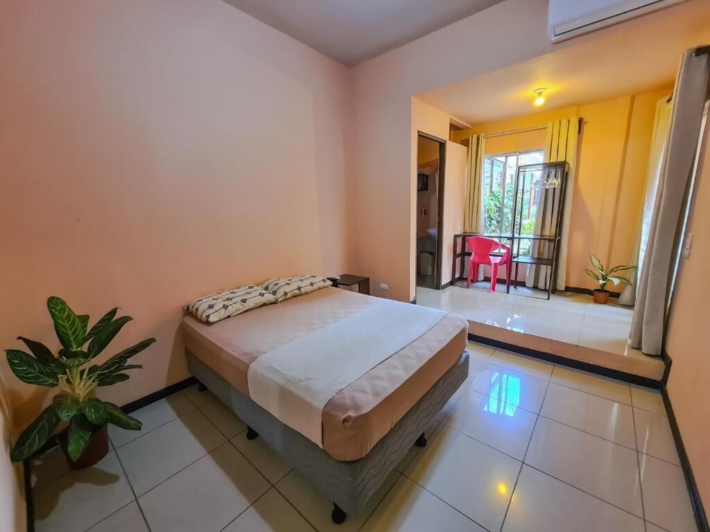 A bedroom with a bed, a potted plant, and a view of a balcony with a chair.