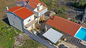 Une maison à deux étages avec un toit recouvert de tuiles rouges, une piscine et un mur en pierre.