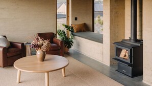 Ein geräumiges Wohnzimmer mit großem Fenster, integriertem Kamin, rundem Holztisch und gemütlicher Sitzecke.