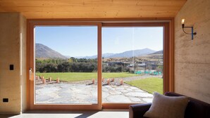 Ein Zimmer mit einer großen Schiebeglasdoor, die auf eine Terrasse mit einem gepflasterten Weg und Blick auf eine Berglandschaft führt.