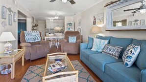 Ein Wohnzimmer mit einem blauen Sofa, zwei Sesseln, einem Couchtisch und einem Essbereich mit einem weißen Tisch und Stühlen.