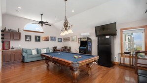 A spacious living area with a pool table, a ceiling fan, and a large window offering a view. - A Speckled Trout: Soundfront, Hot Tub, Game Room, Private Dock (Nags Head)