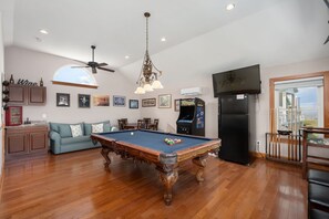 A spacious living area with a pool table, a ceiling fan, and a large window offering a view.
