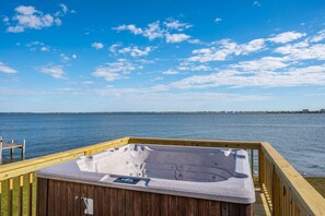Una terraza de madera con un jacuzzi con vista a un cuerpo de agua.