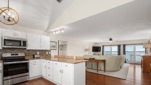 A spacious living area with a kitchen, dining space, and a balcony with a view. - A Speckled Trout: Soundfront, Hot Tub, Game Room, Private Dock (Nags Head)