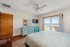 Un dormitorio con cama, cómoda, espejo, ventilador de techo y vista al mar a través de una ventana.
