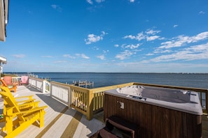 A wooden deck with a hot tub, chairs, and a view of the water.