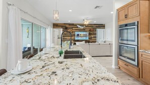 A modern kitchen with a marble countertop, wooden cabinets, and a built-in oven. - Heaven Found!  Stunning River Views & Pool - Villa Island Sunset - Roelens Vacations (Fort Myers)