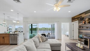 A modern living room with a grey sectional sofa, a wooden coffee table, and a ceiling fan. - Heaven Found!  Stunning River Views & Pool - Villa Island Sunset - Roelens Vacations (Fort Myers)