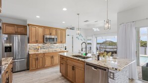 A modern kitchen with wooden cabinets, stainless steel appliances, and a large island with a sink. - Heaven Found!  Stunning River Views & Pool - Villa Island Sunset - Roelens Vacations (Fort Myers)